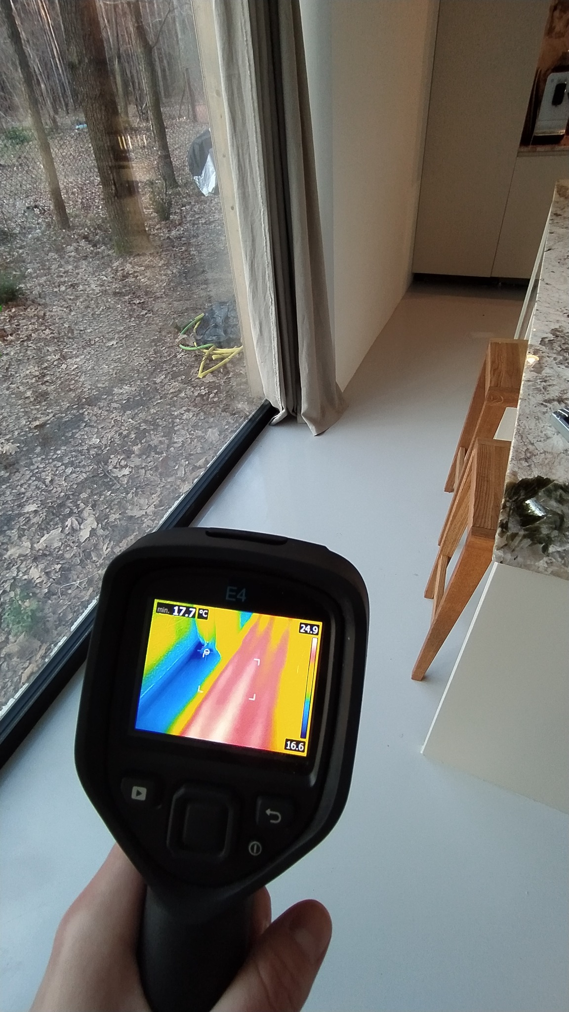 Pomiar termowizyjny okna w nowoczesnym domu, widoczny termogram na ekranie kamery Flir E4, wskazujący na rozkład temperatur w okolicy ramy okiennej.