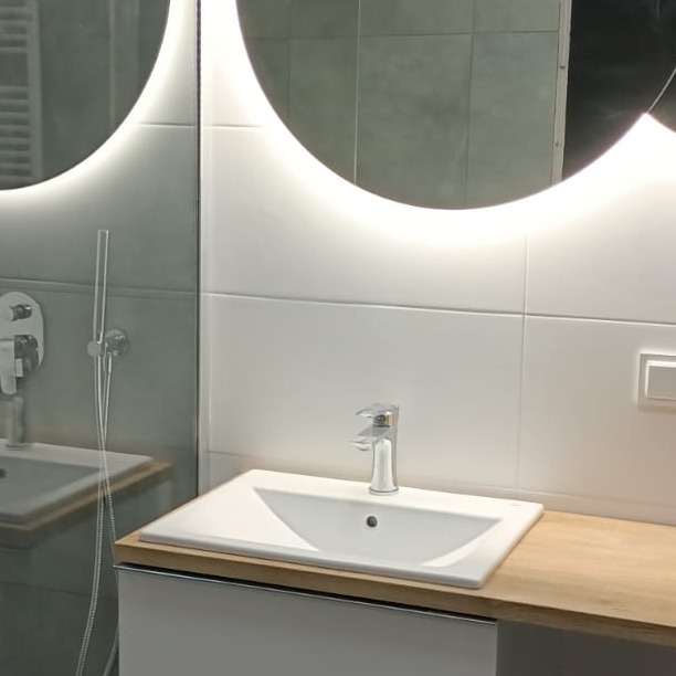 Nowoczesna umywalka nablatowa z chromowaną baterią i podświetlanym lustrem w łazience w Cieplewie, wykończona białymi płytkami.