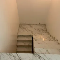 Schody wyłożone białymi płytkami imitującymi marmur, widok z góry, jasne ściany i sufit, minimalistyczny design.