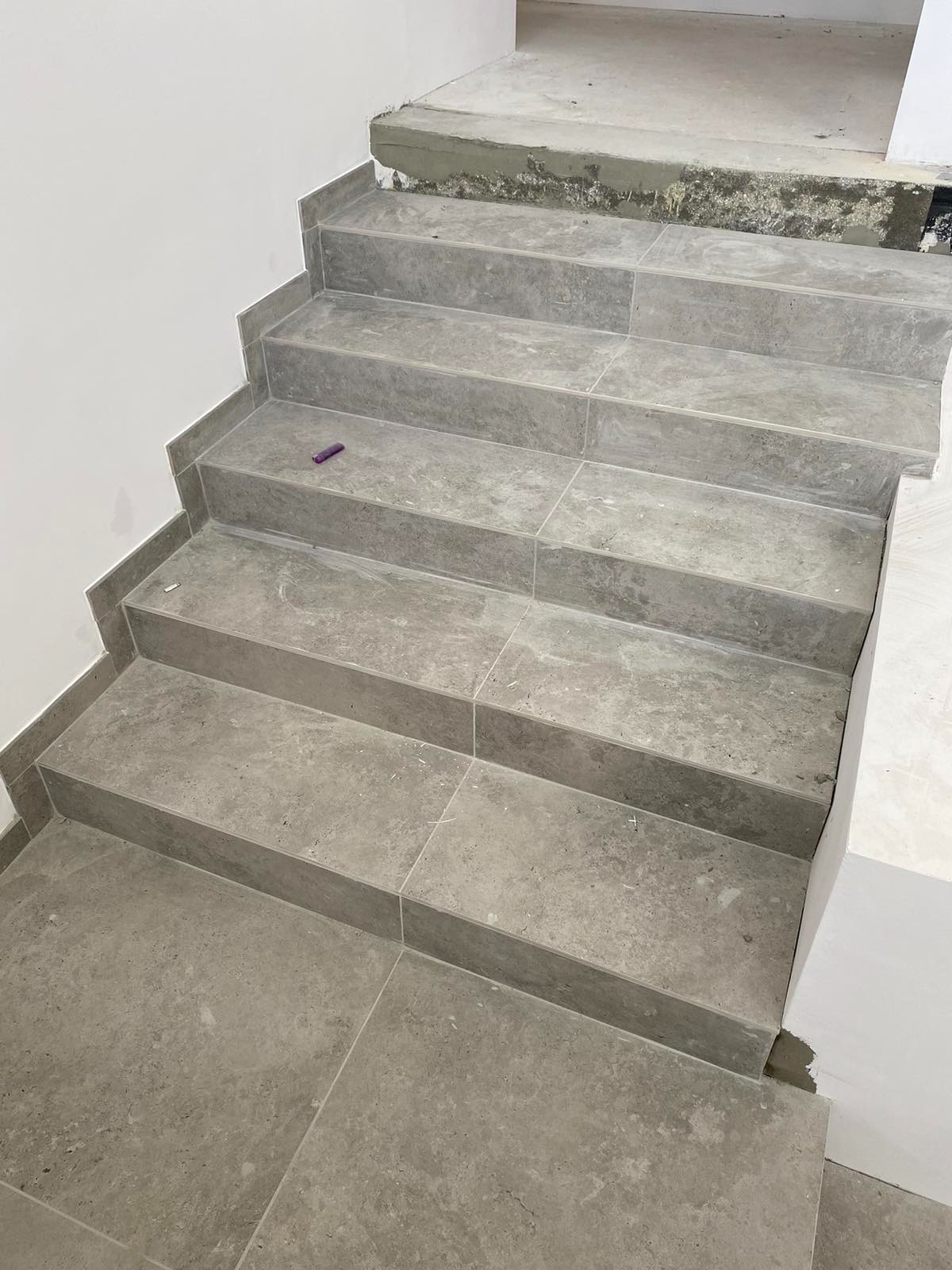 Wyłożone szarymi płytkami schody wewnętrzne w trakcie remontu, widoczna niedokończona krawędź stopnia i fioletowy znacznik na jednym ze stopni.