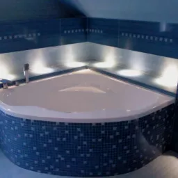 Narożna wanna obudowana mozaiką w odcieniach błękitu i granatu, z podświetleniem wnęki nad wanną, chromowana bateria.