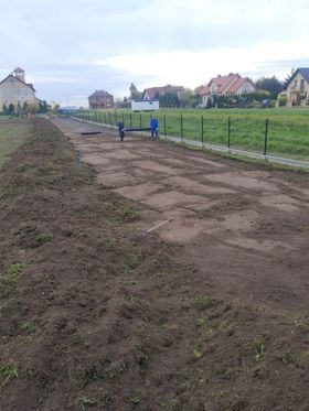 Przygotowany teren pod trawnik z widocznymi śladami po wyrównywaniu, w tle zabudowa jednorodzinna i zielone ogrodzenie z siatki.