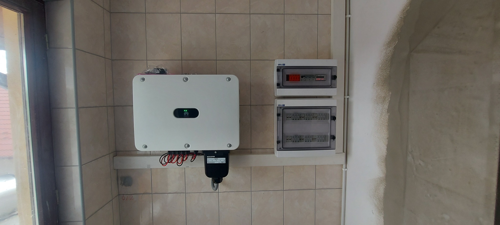 Zamontowany inwerter Huawei z podłączonymi przewodami i zabezpieczeniami elektrycznymi na ścianie wyłożonej płytkami ceramicznymi.
