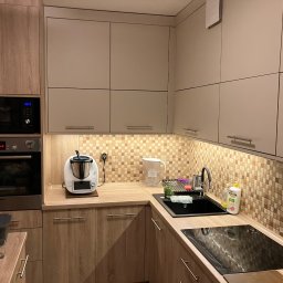 Meble Paweł Król - Jasna kuchnia z drewnianymi szafkami, mozaikową ścianą nad blatem, kuchenką indukcyjną i termomixem.