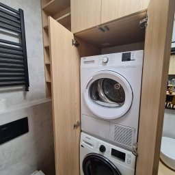 Meble Paweł Król - Pralka i suszarka w zabudowie z jasnego drewna w łazience, widoczne zawiasy i fragment toalety.