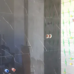 Częściowo wyłożona czarną płytką ściana łazienki z białymi żyłkami, widoczne krzyżyki dystansowe, poziomica i rury instalacyjne w ścianie.