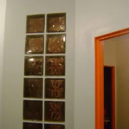 Ściana z wbudowanymi dekoracyjnymi, brązowymi luksferami ułożonymi pionowo, obok pomarańczowe obramowanie drzwi.