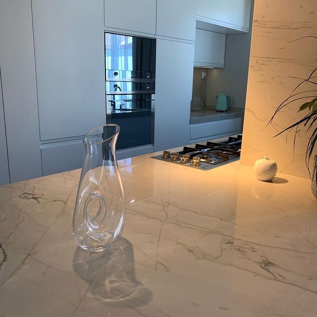 Jasna kuchnia z blatem z białego marmuru, szklanym dzbankiem i minimalistycznym wystrojem.