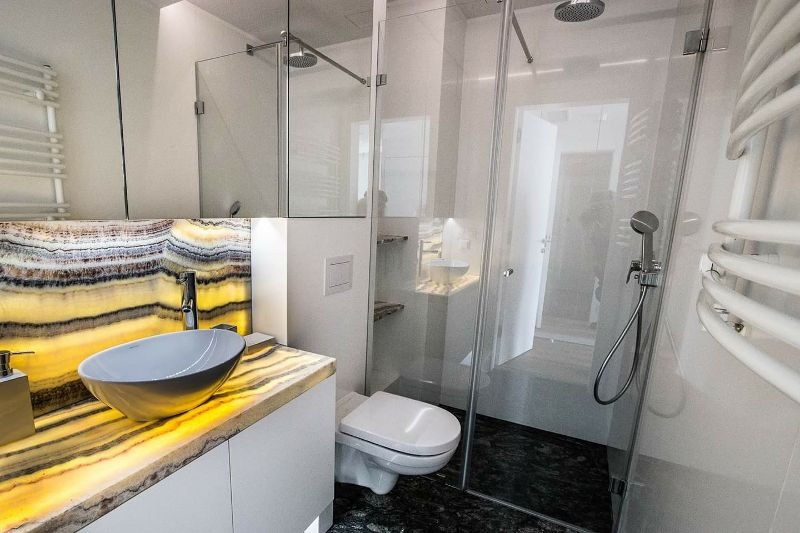 Nowoczesna łazienka z blatem z podświetlanego onyksu, owalną umywalką nablatową i kabiną prysznicową ze szklanymi drzwiami.