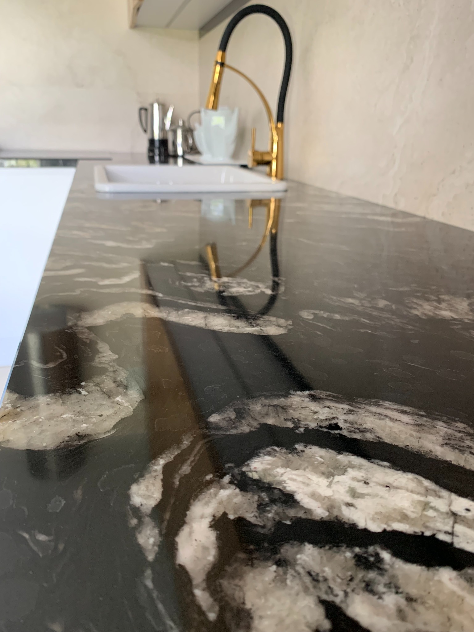 Czarny blat z białymi żyłami, z widocznym złotym kranem i naczyniami kuchennymi w tle.