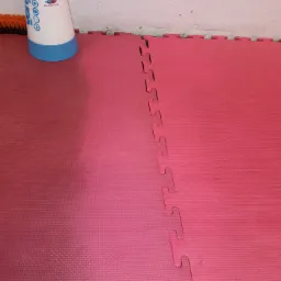 Czerwona mata piankowa po czyszczeniu, widoczna różnica w kolorze po lewej stronie, obok biały opryskiwacz ciśnieniowy z niebieskimi akcentami i szczotka.