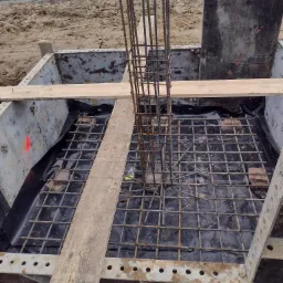 Przygotowanie zbrojenia fundamentu pod budynek w Biłgoraju, widoczne stalowe pręty i szalunek. Na dnie folia izolacyjna.