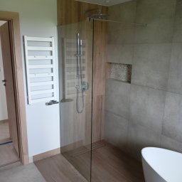 Mateusz Pindel Wykończenia Wnętrz - Nowoczesna łazienka z kabiną prysznicową typu walk-in, grzejnikiem drabinkowym na ścianie, i wolnostojącą wanną, wykończona płytkami w odcieniach beżu i szarości, z akcentem dekoracyjnej niszy.