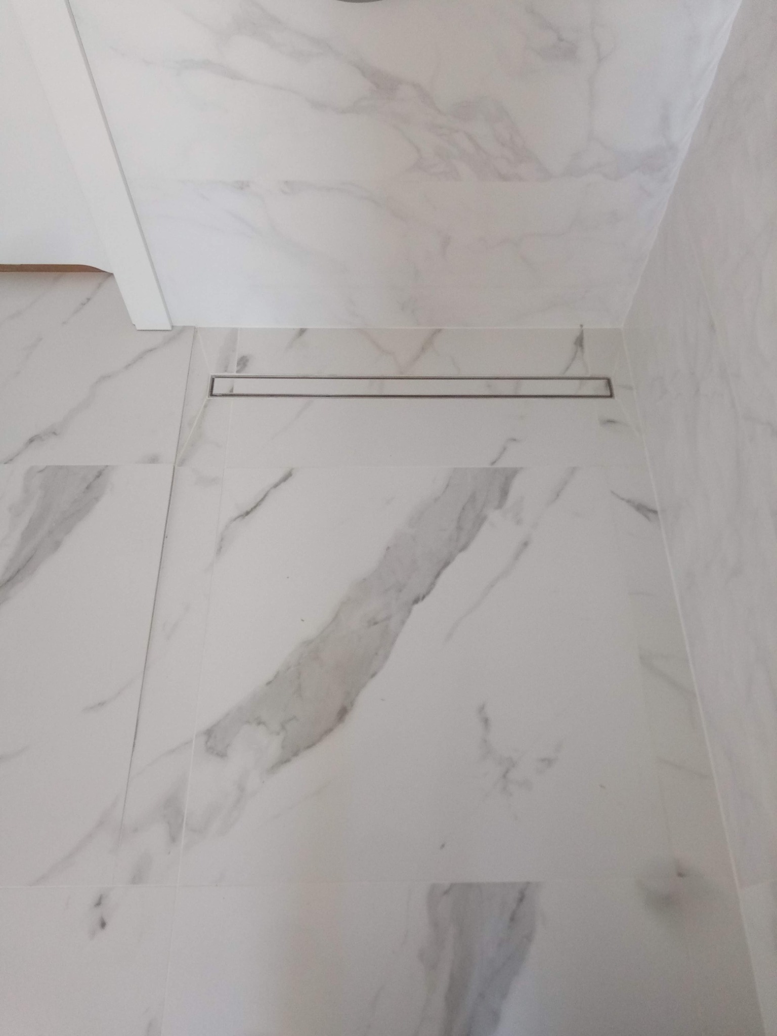 Biała łazienka z marmurowymi płytkami i odpływem liniowym. Minimalistyczny design, jasne wnętrze, nowoczesne wykończenie. Widok z góry.