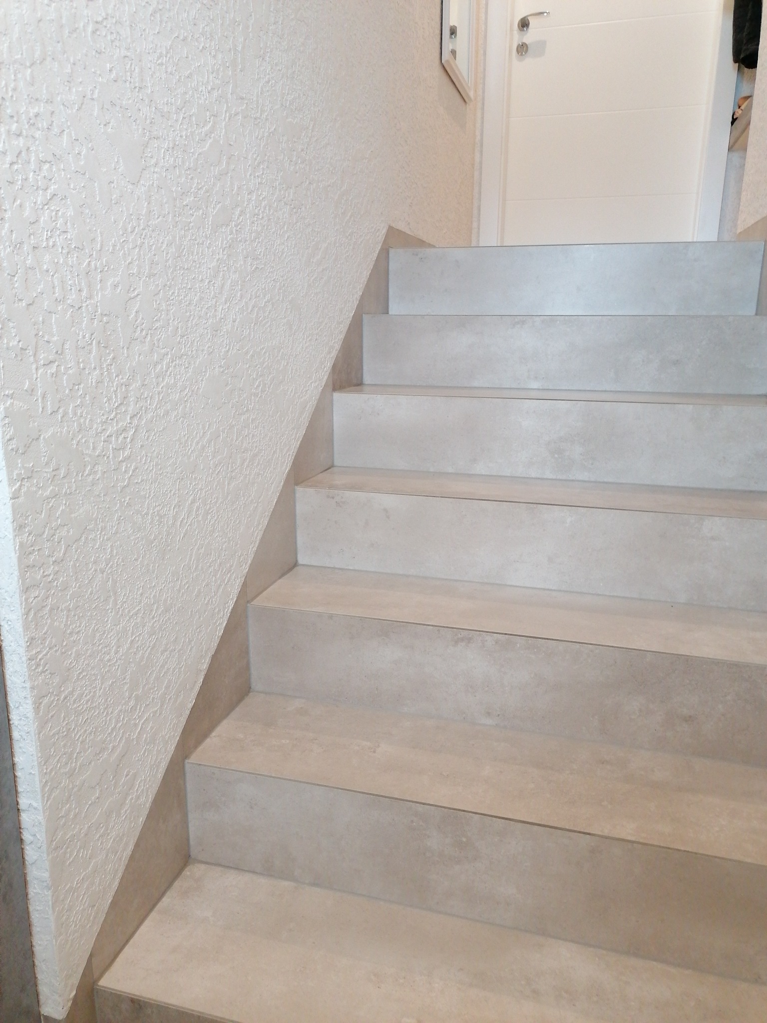 Schody wykończone beżowymi płytkami w domu w Gałkówku, ściana z dekoracyjnym tynkiem, białe drzwi w tle.