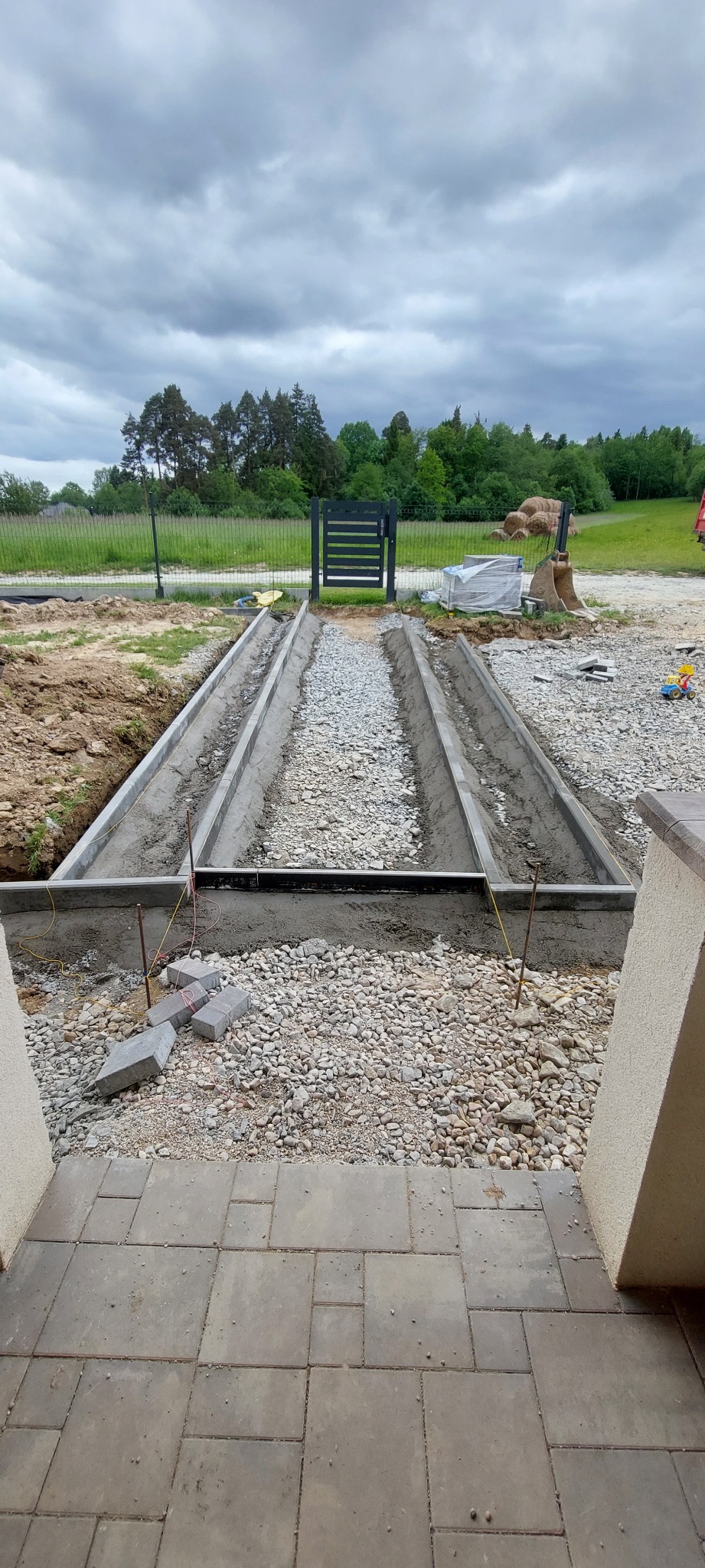 Przygotowanie podłoża pod ścieżkę z kostki brukowej: betonowe obrzeża, podsypka z kamienia, widok z perspektywy ułożonej kostki przy wejściu do domu.