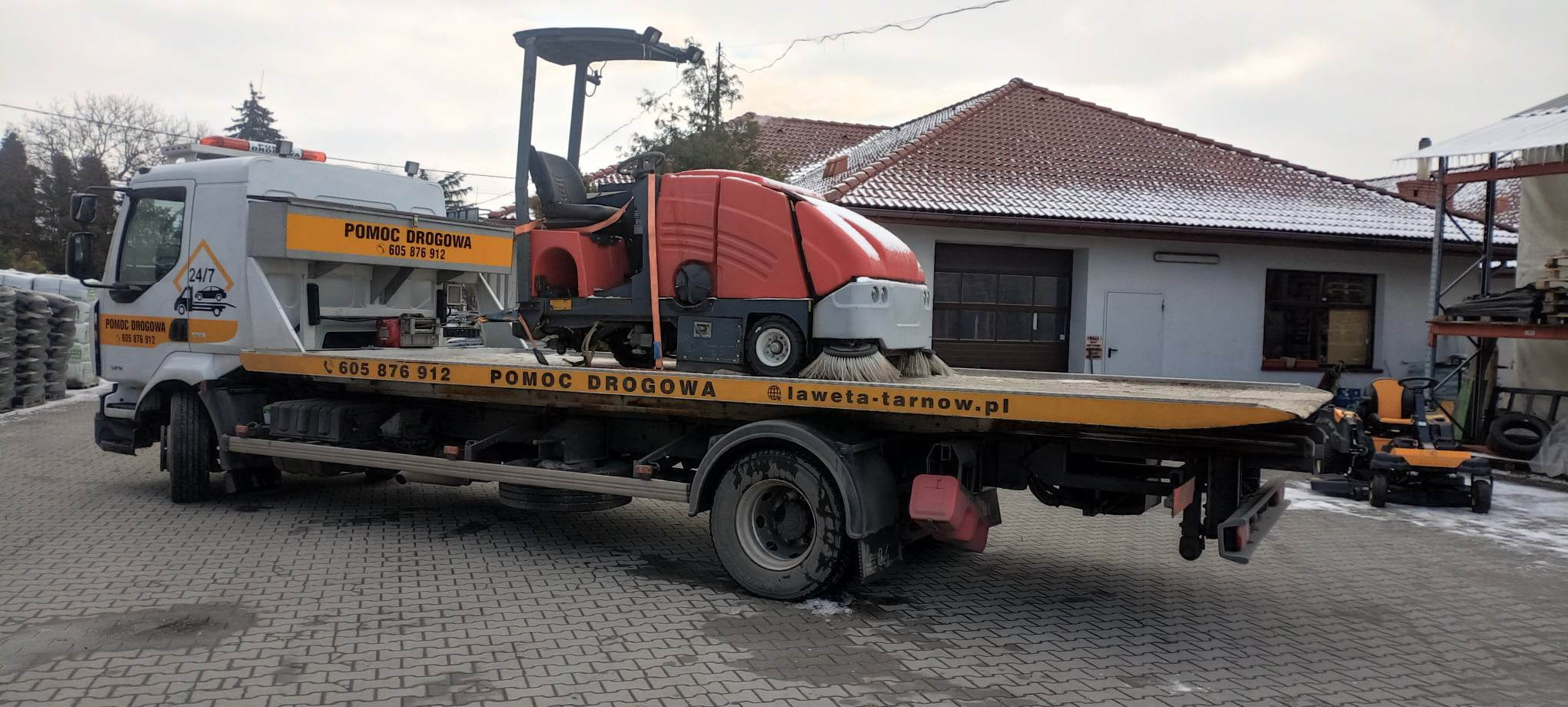 Pomoc drogowa przewozi na lawecie czerwoną zamiatarkę uliczną z obrotowymi szczotkami, widoczny numer telefonu i adres strony internetowej laweta-tarnow.pl