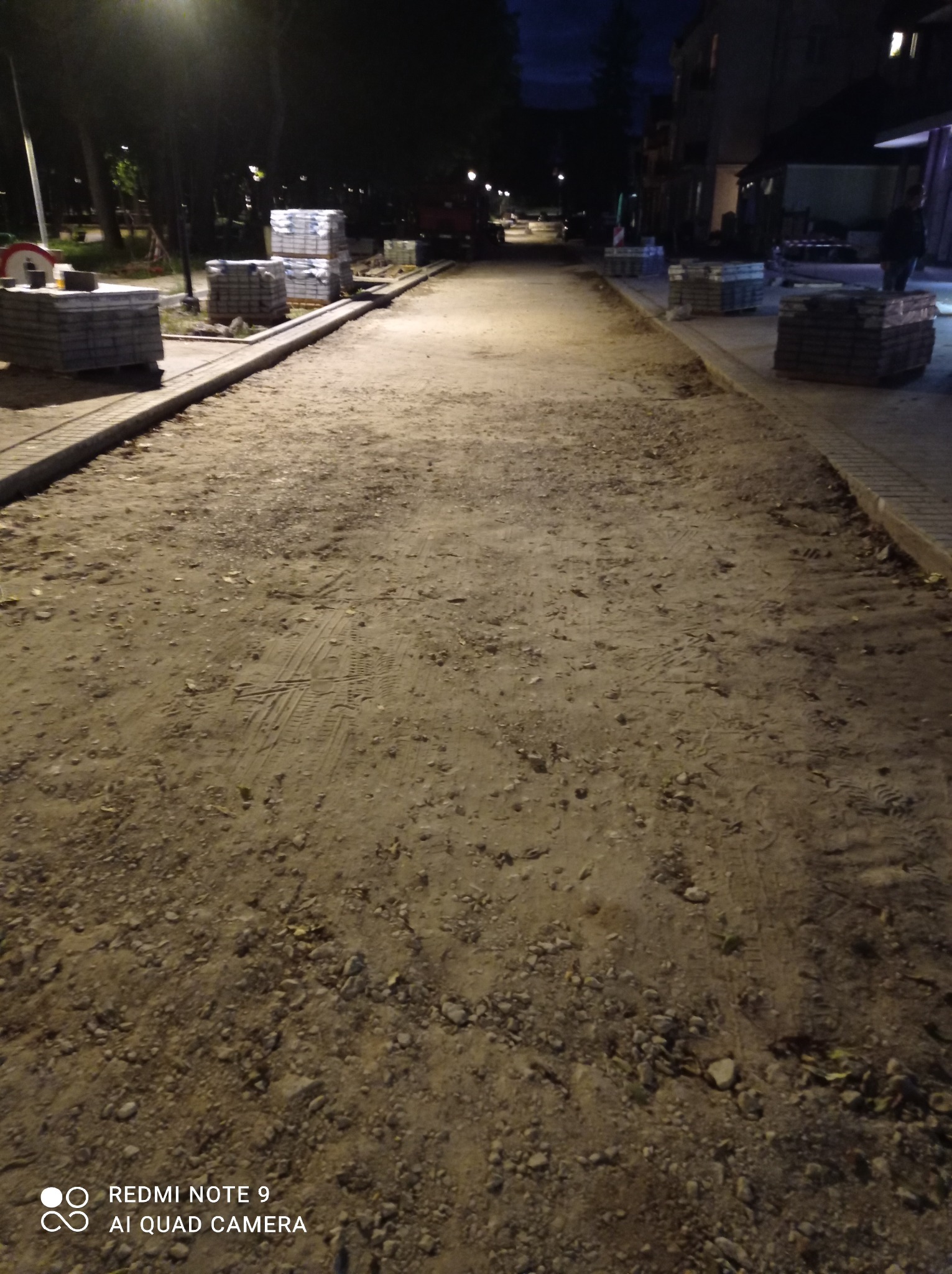 Przygotowanie podłoża pod kostkę brukową w nocy, widoczne ułożone obrzeża, stosy kostki i wyrównany teren z widocznymi śladami opon
