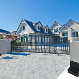 Czarna, ozdobna brama wjazdowa z automatyką na tle luksusowego domu jednorodzinnego w Łodzi, widok na kostkę brukową i zadbany trawnik.