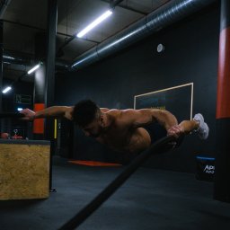 Łukaszgórnisiewicz - Mężczyzna w trakcie ćwiczenia równowagi na linie w siłowni, z napiętymi mięśniami i skupionym wzrokiem.