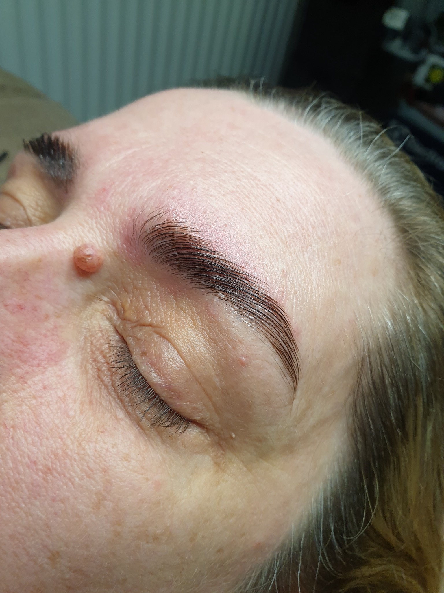 Zbliżenie na kobiecą twarz z widocznymi, świeżo po zabiegu, ciemnymi brwiami o idealnym kształcie, skóra z widocznym znamieniem