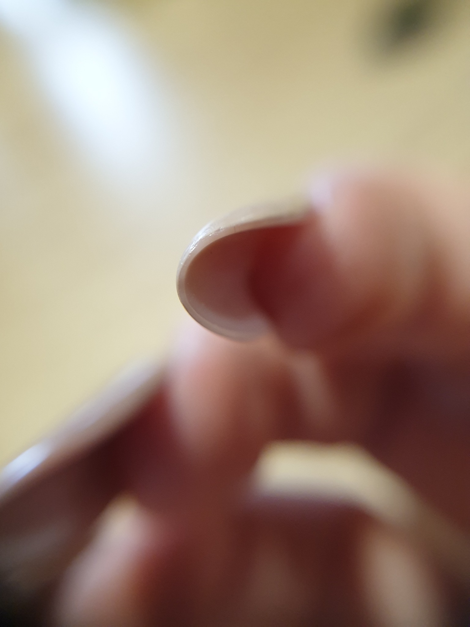 Zbliżenie na beżowy, zaokrąglony paznokieć z widoczną strukturą żelu, na tle rozmytej skóry palca.