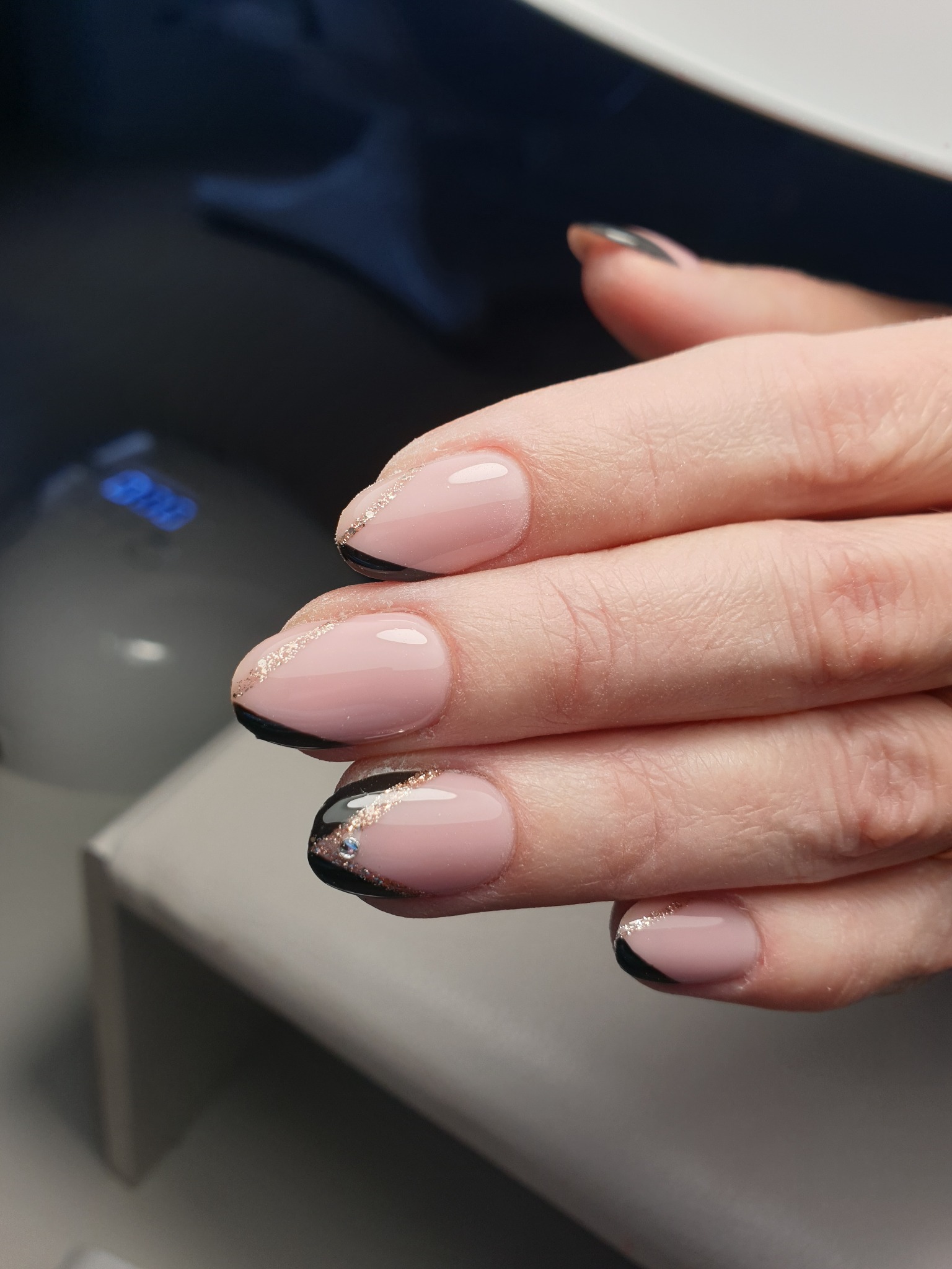 Delikatne, różowe paznokcie z czarnym półksiężycem przy nasadzie i drobną, złotą linią brokatu