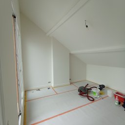 Myjnia Parowa Wash - Pokój ze skośnym sufitem po świeżym pomalowaniu na biało, zabezpieczony folią malarską i taśmą. Widoczne narzędzia malarskie i odkurzacz.