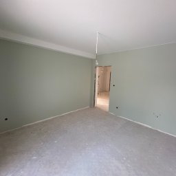 Myjnia Parowa Wash - Pusty pokój po malowaniu ścian na delikatny odcień zieleni, widoczne ślady po gładzi na podłodze i wystająca żarówka z sufitu.