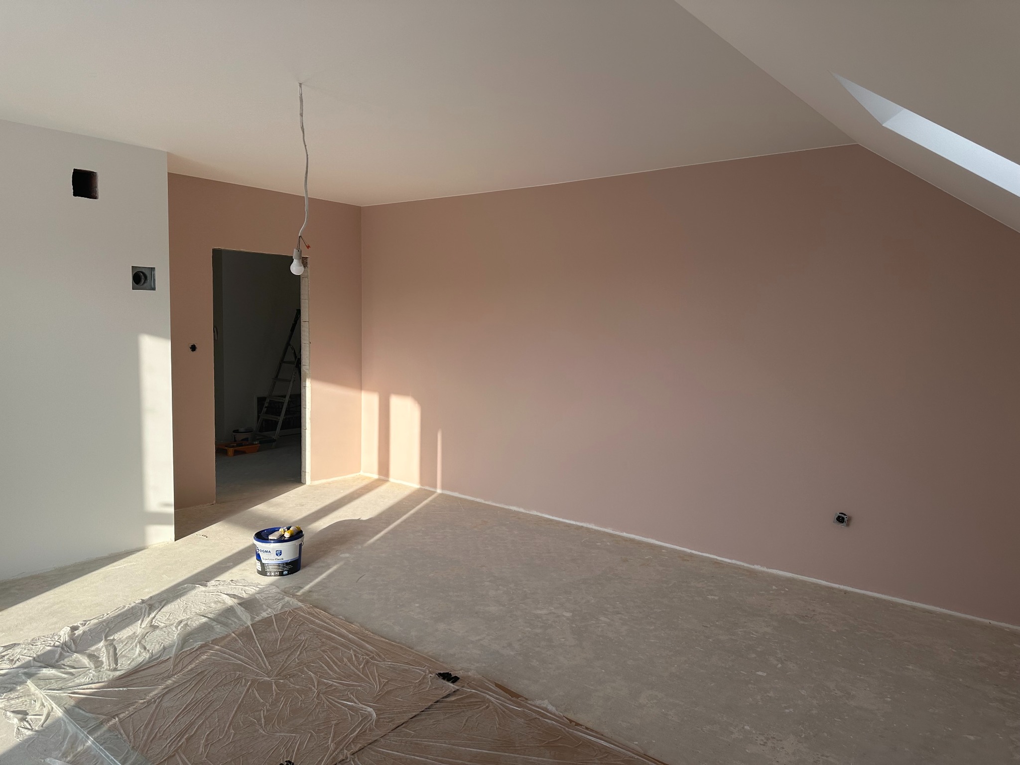 Pokój po częściowym odmalowaniu na kolor różowy, widoczne zabezpieczenie podłogi folią, puszka z farbą i drabina w tle.