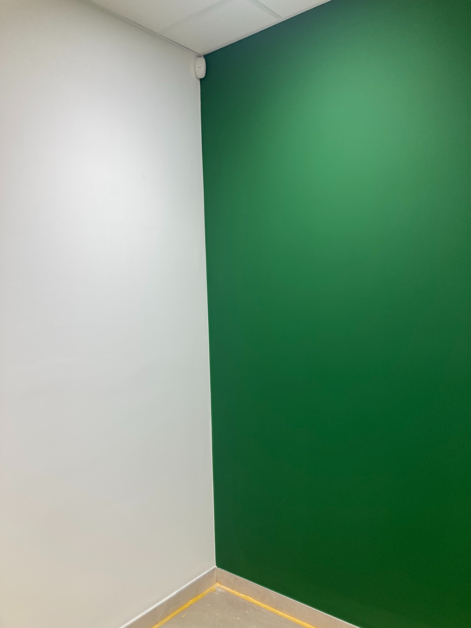 Wnętrze po remoncie: ściana pomalowana na biało i zielono, widoczna taśma malarska na podłodze.