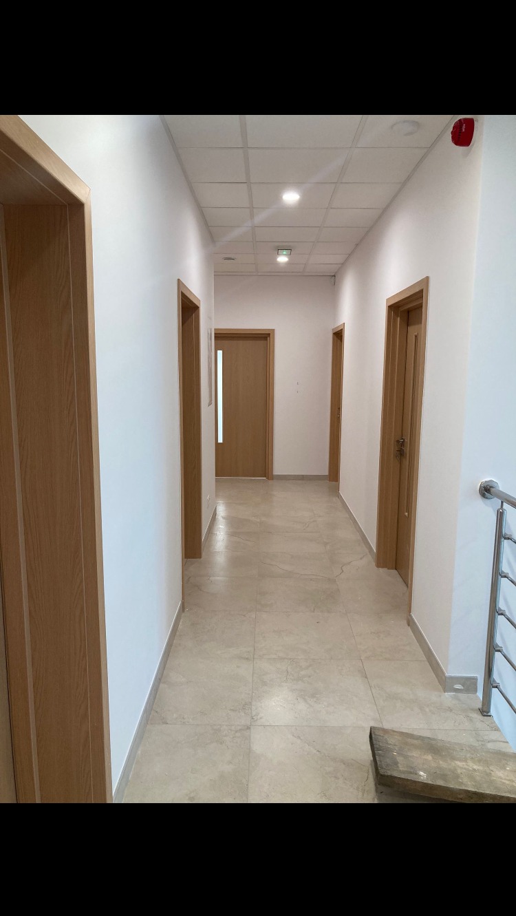 Korytarz biurowy po malowaniu, z drewnianymi drzwiami i beżową podłogą z płytek, widoczny fragment rusztowania przy schodach.