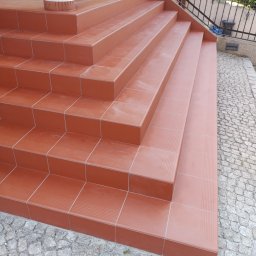Volodymyr Gonchar - Zewnętrzne schody wejściowe wyłożone terakotą z delikatnym wzorem, obok kostka brukowa i czarna metalowa balustrada.