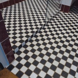 Volodymyr Gonchar - Ukończona podłoga łazienki wyłożona czarno-białą szachownicą, z widocznym fragmentem szklanej kabiny prysznicowej i brązowym pasem płytek przy ścianie.