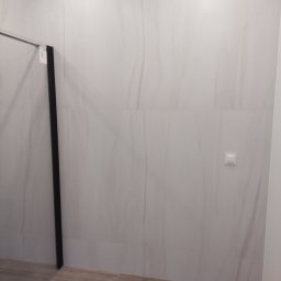 Volodymyr Gonchar - Wykończona łazienka z dużymi, jasnymi płytkami imitującymi marmur na ścianach, drewnopodobną podłogą i czarną ramą szklanej kabiny prysznicowej.