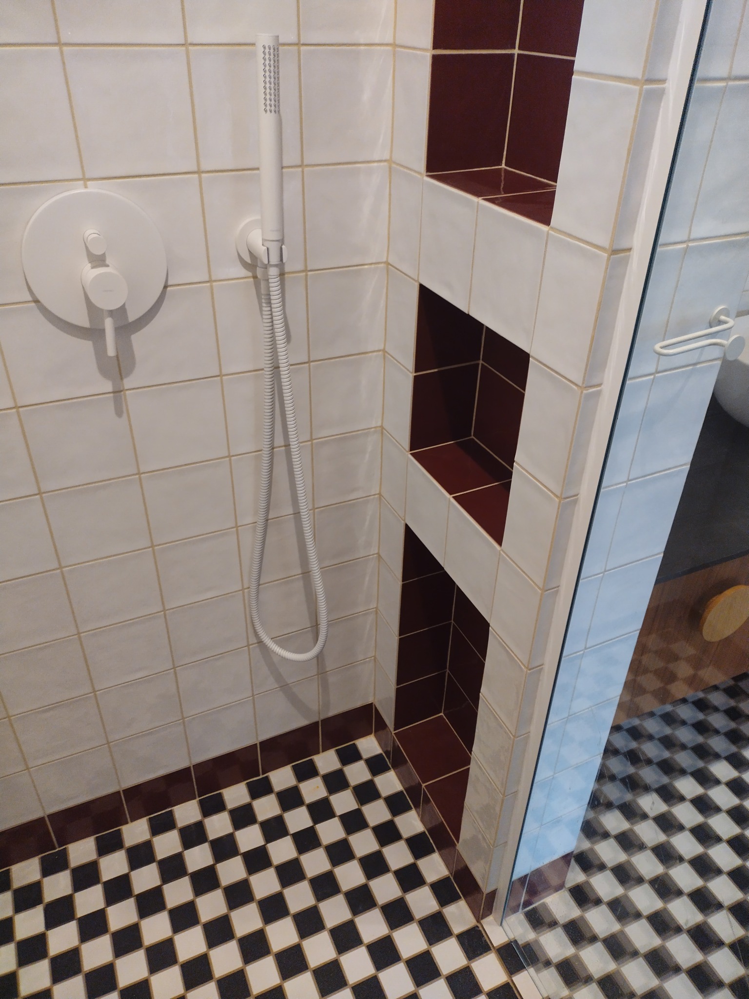 Nowoczesna kabina prysznicowa we Wrocławiu z biało-brązowymi płytkami, z wnękami na kosmetyki wyłożonymi brązowymi płytkami i czarno-białą szachownicą na podłodze.