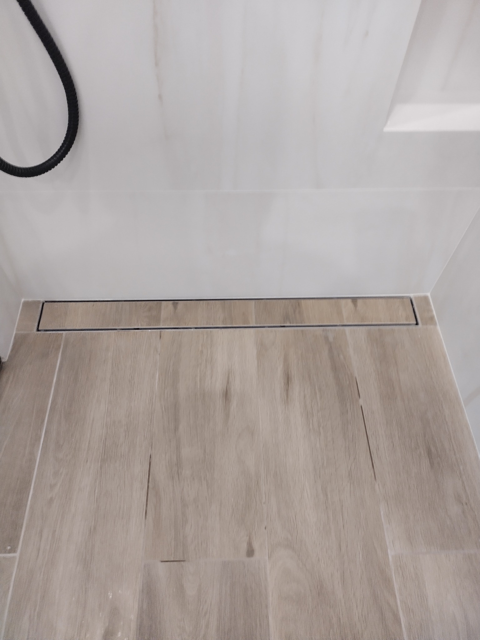 Ukończona łazienka z podłogą imitującą drewno i liniowym odpływem prysznicowym w kolorze czarnym, widok z góry.