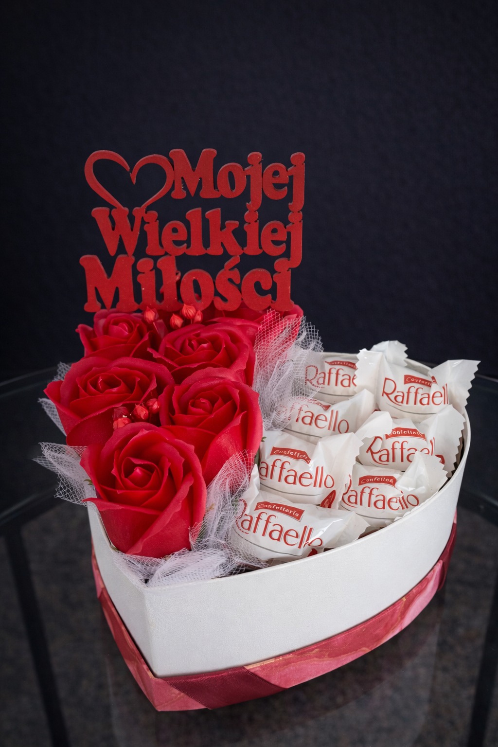 Kompozycja w kształcie serca: czerwone róże i Raffaello, z topperem 'Mojej Wielkiej Miłości'. Idealne na walentynki lub rocznicę, na ciemnym tle.