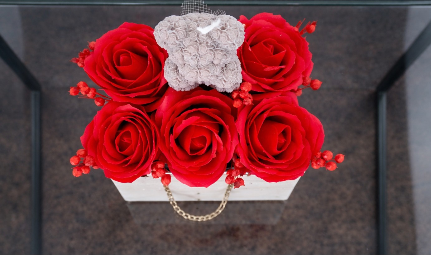 Dekoracja stołu: czerwone róże i szary miś w białym pudełku z łańcuszkiem, widok z góry, elegancka kompozycja na imprezę.