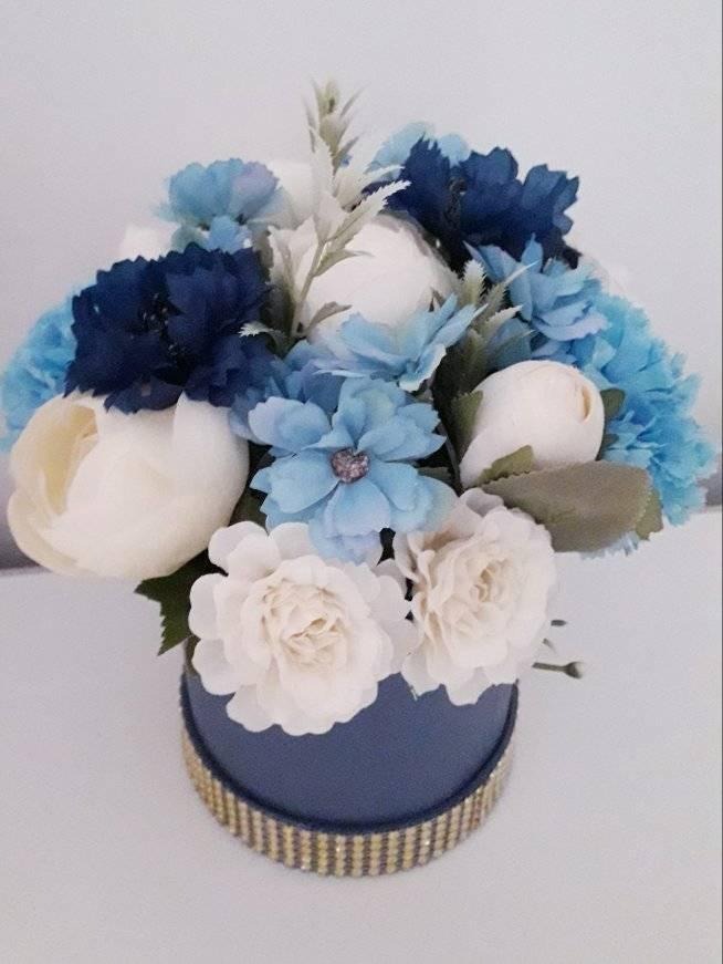 Dekoracyjny bukiet sztucznych kwiatów w odcieniach bieli i błękitu, umieszczony w granatowym pudełku ozdobionym złotymi cyrkoniami.