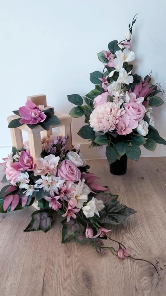 Kompozycja kwiatowa w jasnych odcieniach różu i bieli, umieszczona w drewnianej latarence oraz w czarnym wazonie, na drewnianej podłodze.