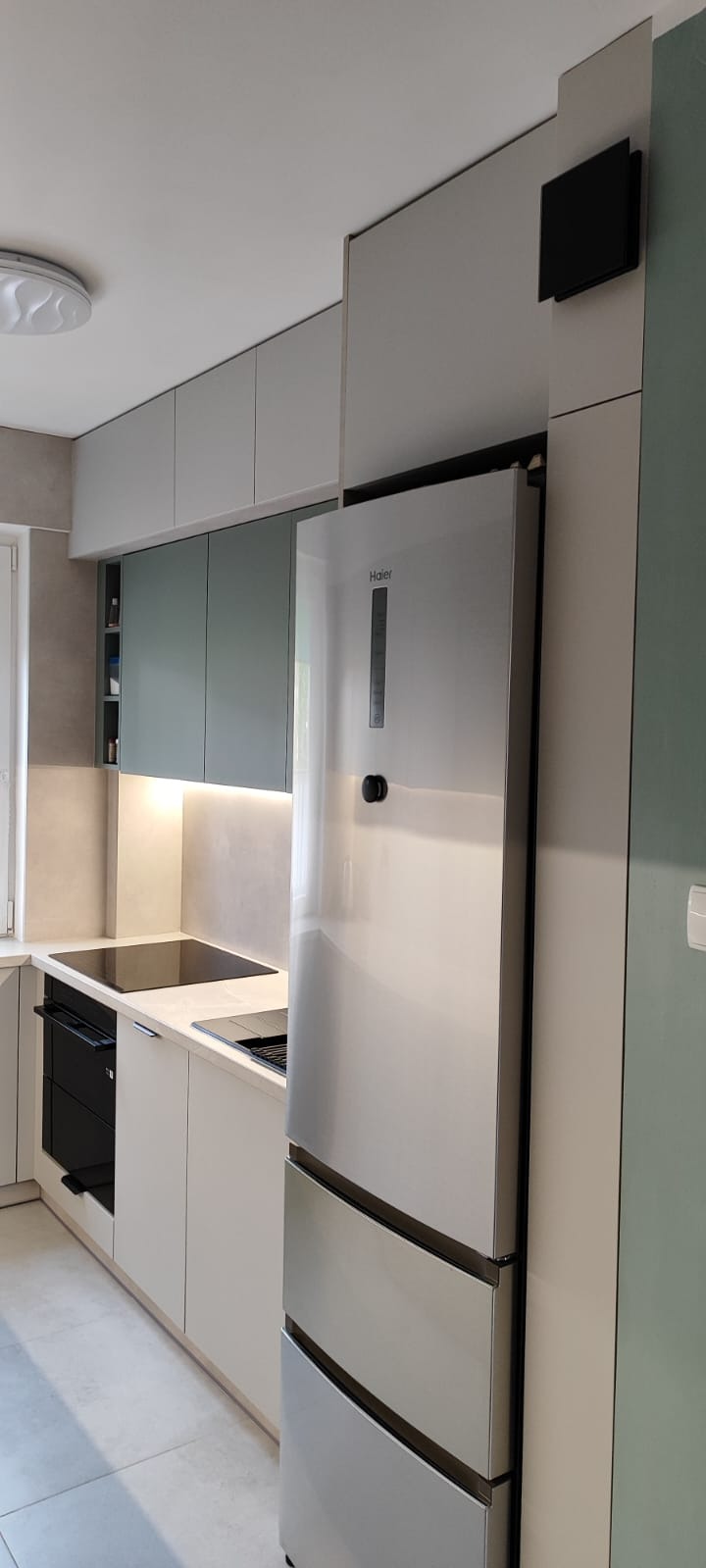 Nowoczesna kuchnia z szarymi i białymi szafkami, oświetleniem LED pod szafkami wiszącymi i srebrną lodówką Haier. Minimalistyczny design.