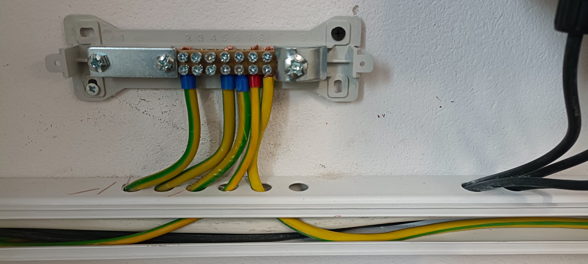 Złącze wyrównawcze potencjałów z przewodami ochronnymi i roboczymi, zamocowane na ścianie wewnątrz listwy instalacyjnej.