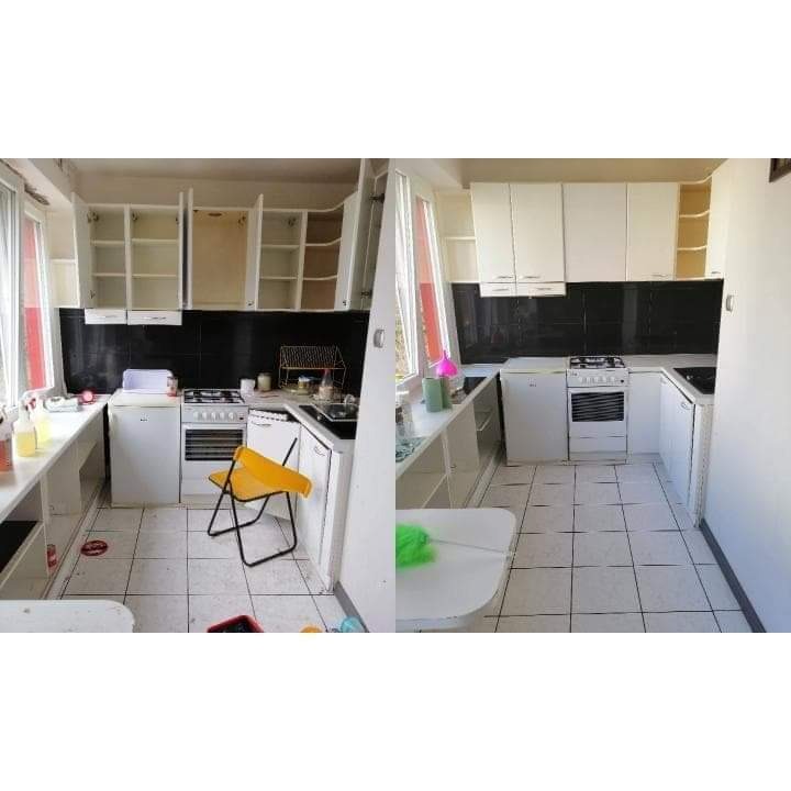 Kuchnia przed sprzątaniem: białe szafki z otwartymi drzwiczkami, czarny panel nad blatem, biała podłoga w kwadratowe płytki, żółte krzesło składane, widoczne środki czystości i akcesoria.