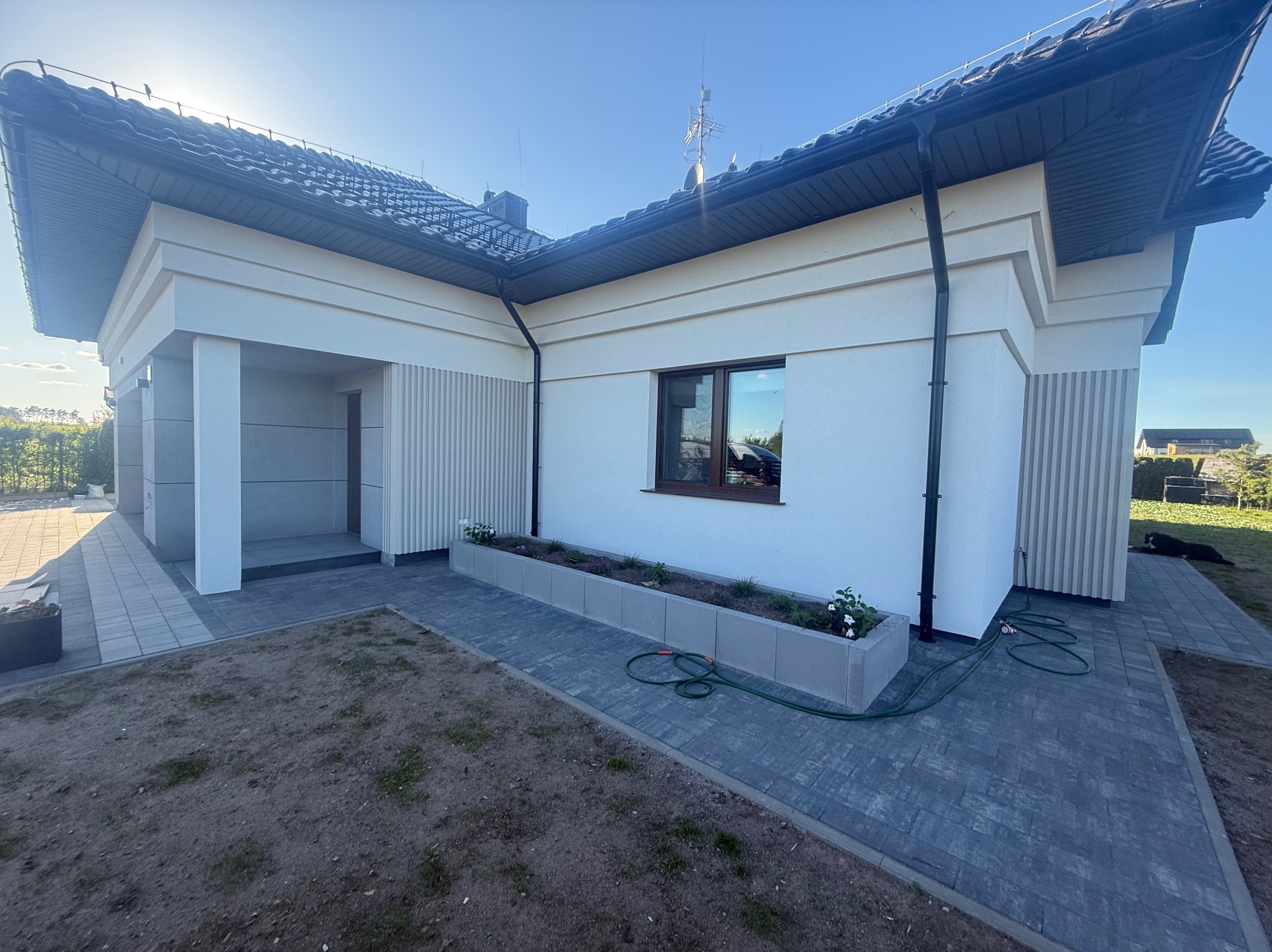 Elewacja domu jednorodzinnego w jasnych barwach z elementami dekoracyjnymi. Widoczne wykończone ściany, okna i kostka brukowa na podjeździe.