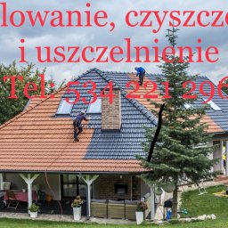 AllMar Marcin Moczulski - Dwóch pracowników na dachu domu podczas malowania dachówki na dwa kolory: czerwony i grafitowy. Widoczny fragment elewacji domu z oknami i tarasem. Na pierwszym planie drzewo iglaste.