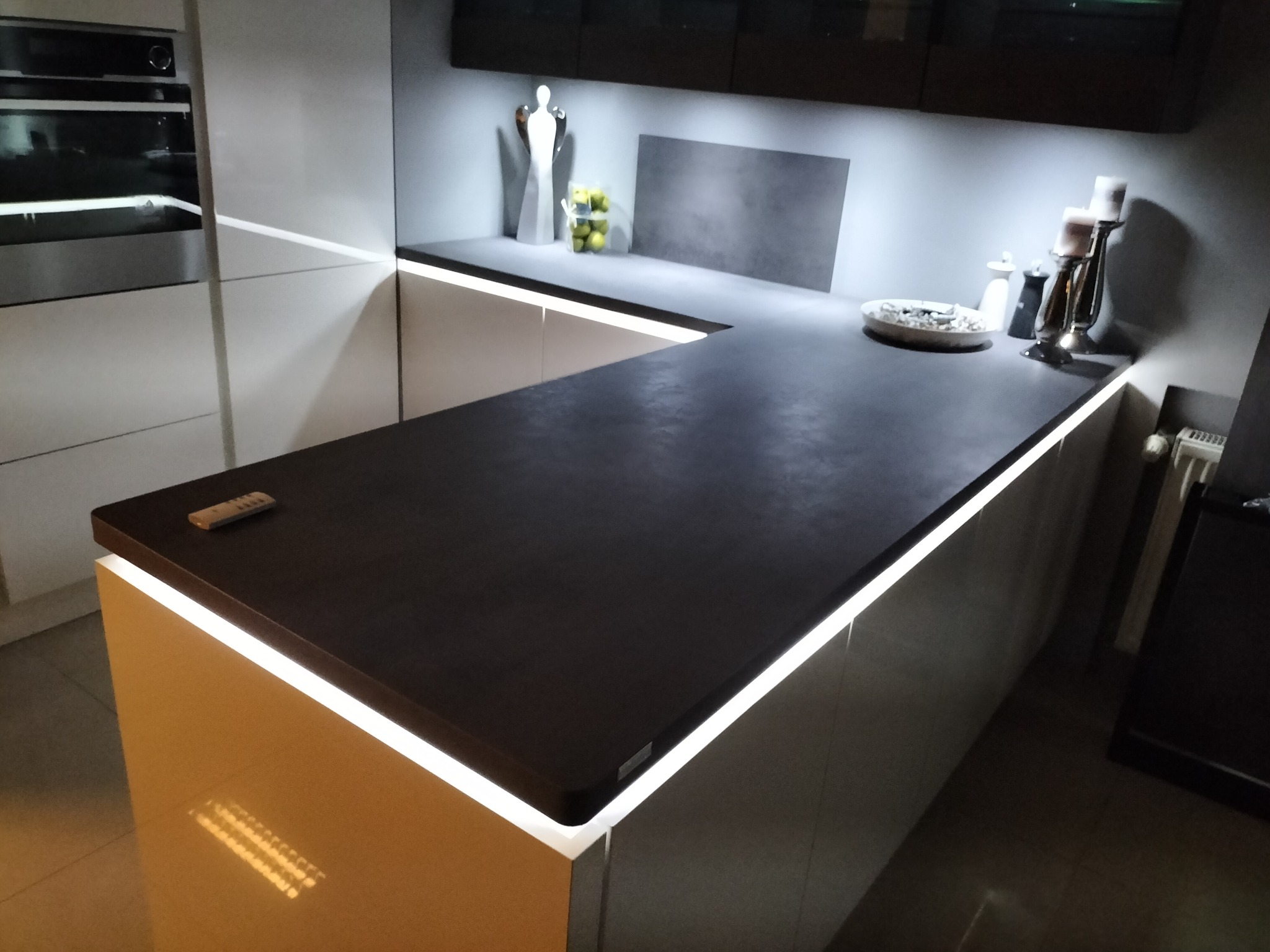 Nowoczesna kuchnia z ciemnym blatem, podświetleniem LED i elementami dekoracyjnymi, takimi jak figurka anioła i świeczniki.