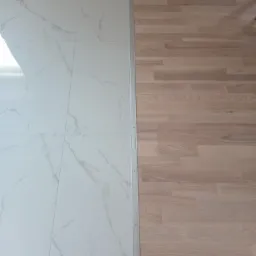 Połączenie podłogi z jasnych paneli drewnianych i białych płytek imitujących marmur, oddzielonych srebrną listwą progową.