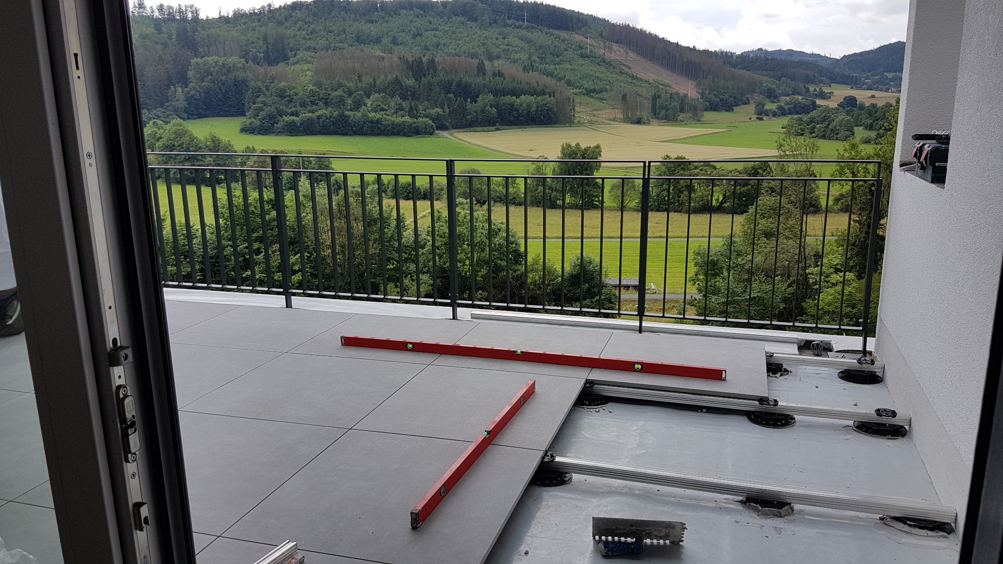 Montaż płytek na tarasie z widokiem na zielone wzgórza, poziomice wskazują na precyzję prac, widoczne elementy konstrukcyjne pod płytkami.