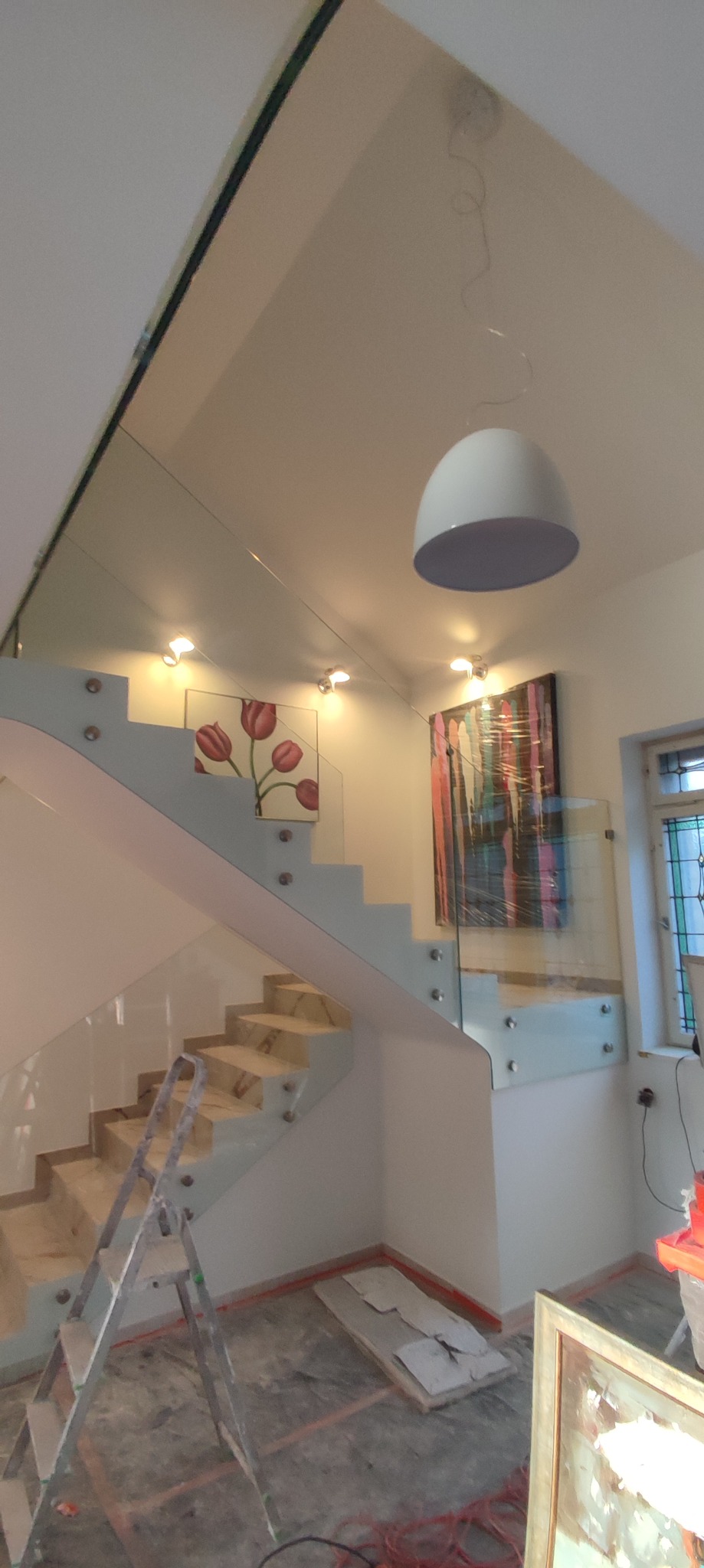 Montaż szklanej balustrady schodowej z marmurowymi stopniami, widoczny aluminiowy profil i drabina malarska.